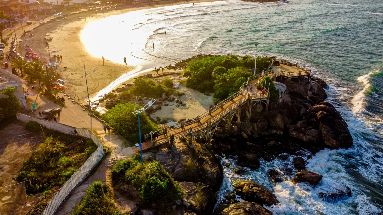 Vista aérea de praia e passarela sobre formações rochosas em Itapoá
